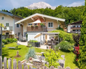 Charmantes Haus mit gepflegtem Garten, Terrasse und Balkon, umgeben von grüner Natur und Bergen.