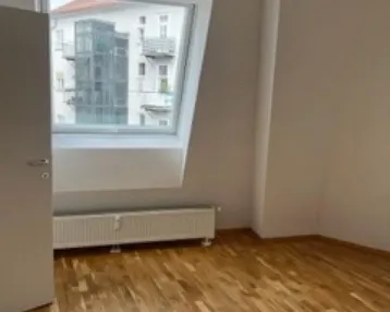Helles Zimmer mit Dachschrägenfenster, Holzboden und Blick auf umliegende Gebäude.