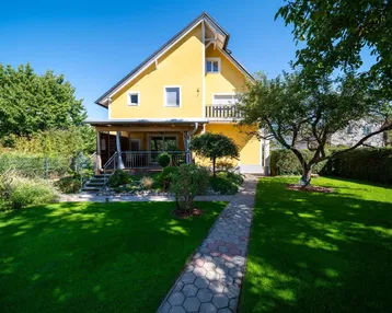 Rückansicht des Hauses mit überdachter Terrasse und einem gepflasterten Weg durch den Garten.
