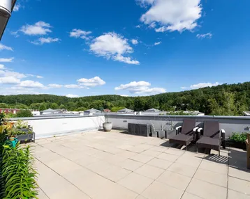 Große Dachterrasse mit bequemen Lounge-Möbeln und weitem Blick ins Grüne unter blauem Himmel.