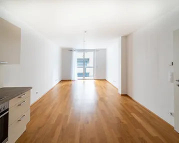 Heller, offener Wohnbereich mit Parkettboden, integrierter Küchenzeile und Zugang zum Balkon.