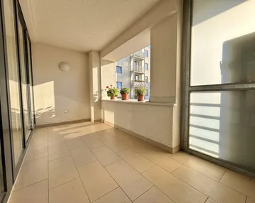 Heller Balkon mit Fliesenboden und Blick auf umliegende Gebäude, ideal für Pflanzen.