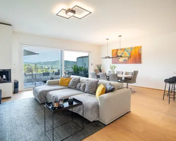 Helles, offenes Wohn-Esszimmer mit modernem Sofa, Kamin und Zugang zur Terrasse mit Seeblick.