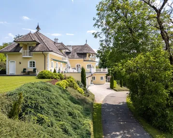 Elegante Villa mit gelber Fassade, weitläufiger Auffahrt und gepflegtem Gartenbereich.