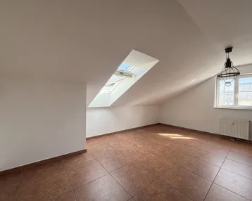 Helles Dachgeschosszimmer mit Dachschräge, Fliesenboden und einem großen Oberlicht.