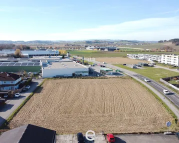 Luftaufnahme eines großen unbebauten Grundstücks umgeben von Wohn- und Gewerbegebäuden mit Fernblick.