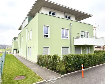 Modernes Mehrfamilienhaus mit hellgrüner Fassade, Balkonen und Flachdach in ländlicher Umgebung.