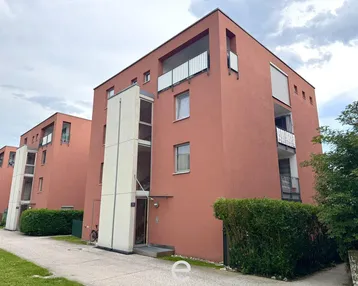 Modernes Mehrfamilienhaus mit roter Fassade und Balkonen unter bewölktem Himmel.
