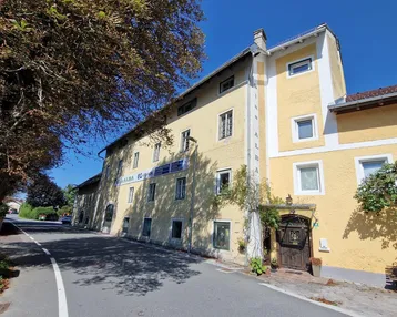 Gelbes Gebäude mit traditioneller Architektur, umgeben von Bäumen und einer Straße unter blauem Himmel.