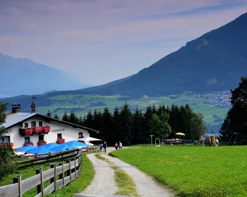 Traditionelles Gasthaus in den Bergen mit blauen Sonnenschirmen und weitem Blick auf die grüne Landschaft.