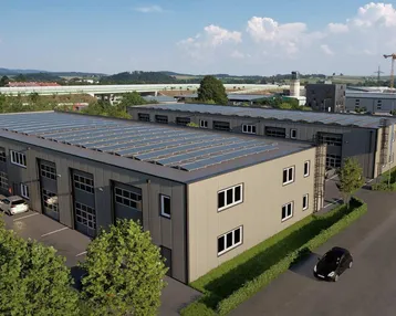 Moderne Gewerbeimmobilie mit Photovoltaikanlage auf dem Dach, umgeben von grüner Landschaft und Parkplätzen.