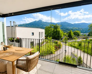 Helles, verglastes Balkon mit Esstisch und Stühlen, bietet einen weiten Bergblick.