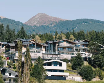 Moderne Gebäude in einer malerischen Berglandschaft mit üppigem Grün und klarem Himmel.