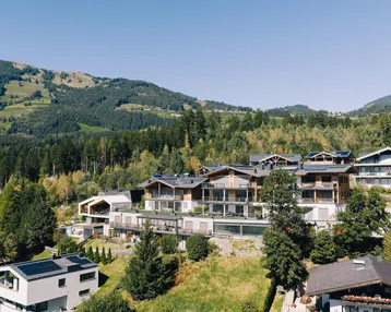 Panoramablick auf eine moderne Wohnanlage in den Bergen mit viel Grün und Wald.