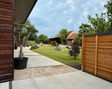 Blick auf den gepflegten Gartenbereich mit Bäumen und einem modernen Gebäude unter einem bewölkten Himmel.
