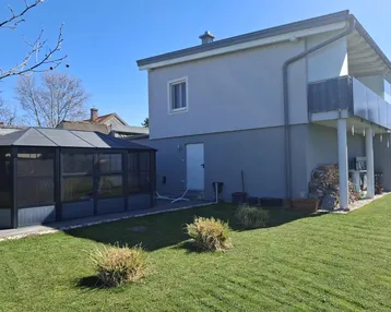 Modernes Haus mit gepflegtem Rasen, einem Wintergarten und einem kleinen Balkon im Obergeschoss.