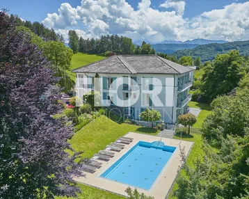 Großzügige Außenanlage mit Pool, Liegewiese und Bergblick, umgeben von viel Grün.
