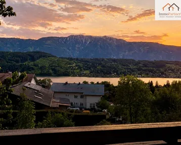 Malerischer Sonnenuntergang über dem See mit Bergblick und Häusern im Vordergrund.