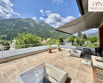 Geräumige Sonnenterrasse mit Fliesenboden, Markise und beeindruckendem Bergblick auf die umliegenden Berge.