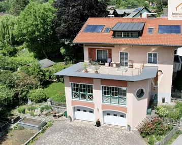 Luftaufnahme eines gepflegten Hauses mit großer Sonnenterrasse, Doppelgarage und weitläufigem Garten.