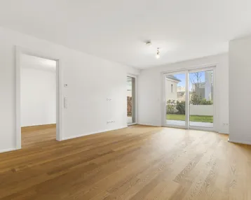 Helles, leeres Wohnzimmer mit Parkettboden und direktem Zugang zum privaten Gartenbereich.