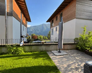 Gepflegter Gartenbereich mit Terrasse und Blick auf die umliegenden Berge, umgeben von modernen Gebäuden.