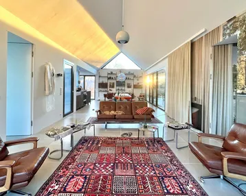 Geräumiges Wohnzimmer mit hohen Decken, großen Fenstern und gemütlichen Ledersofas.