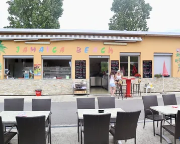Gebäude mit "Jamaica Beach" Beschriftung und davorliegendem Außenbereich mit Tischen und Stühlen.