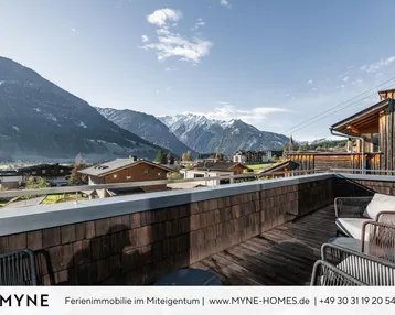 Sonniger Außenbereich mit Sitzgelegenheiten und weitem Blick über das Tal und die umliegende Berglandschaft.