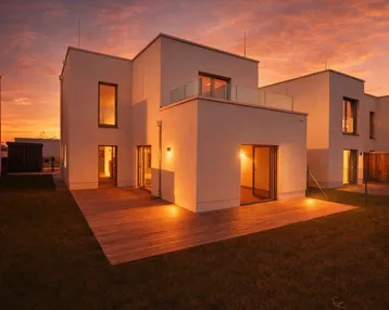 Modernes Einfamilienhaus mit Holzterrasse und Balkon, beleuchtet vom warmen Licht des Sonnenuntergangs.