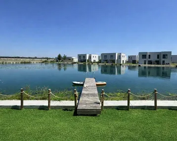 Blick über den gepflegten Rasen und den Steg auf den See mit modernen Häusern am Ufer.