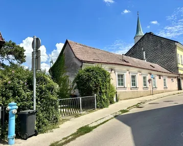 Historisches Gebäude mit rosa Fassade und begrünten Wänden an einer leicht ansteigenden Straße.