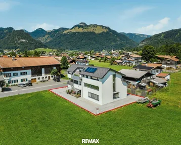 Luftaufnahme eines modernen Hauses mit Photovoltaikanlage und Bergblick in ländlicher Umgebung.