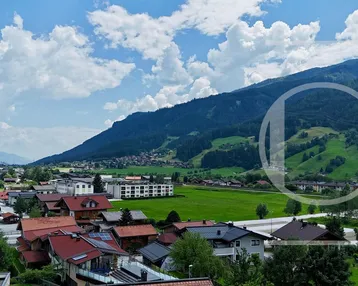 Weitläufiger Panoramablick über ein grünes Tal mit einem Dorf und bewaldeten Bergen unter einem bewölkten Himmel.