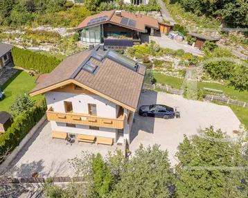 Luftaufnahme eines modernen Hauses mit Satteldach, Balkonen und großem Vorplatz in grüner Umgebung.