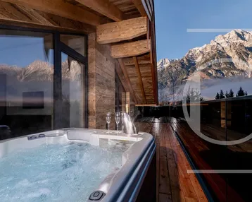 Geräumige Holzterrasse mit Whirlpool und atemberaubendem Bergblick unter blauem Himmel.