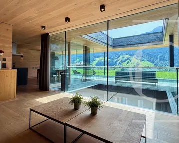 Helles Wohnzimmer mit Holzelementen, großen Glasfronten und beeindruckendem Bergblick.