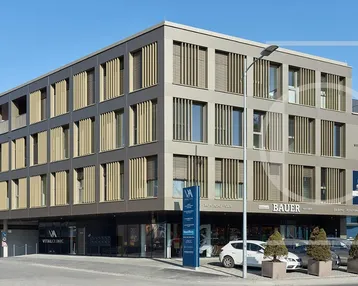 Modernes Geschäfts- und Wohngebäude mit klarer Architektur und vielen Fenstern in städtischer Umgebung.