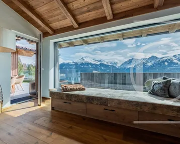 Gemütlicher Wohnbereich mit großer Fensterfront, Holzbalkendecke und atemberaubendem Bergblick.