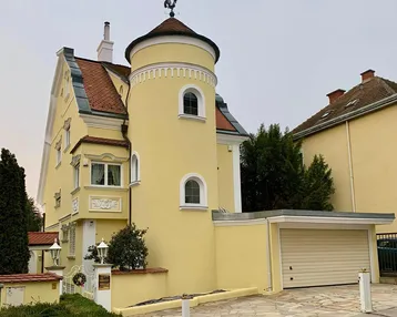 Charmantes gelbes Haus mit markantem Turm, Garage und gepflegtem Vorgarten.