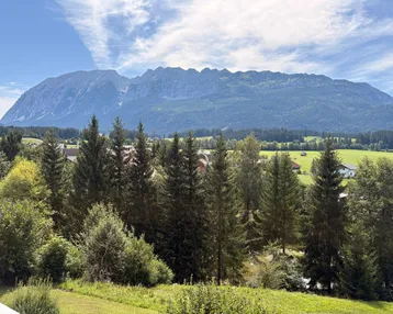 Panoramablick auf die majestätischen Berge und die umliegende grüne Landschaft mit Nadelbäumen.