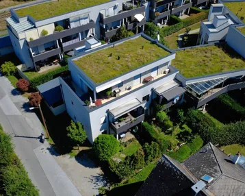 Luftaufnahme moderner Wohngebäude mit begrünten Dächern, Balkonen und gepflegten Gärten in einer Wohnsiedlung.