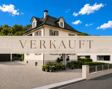 Elegante Stadtvilla mit gepflegtem Vorgarten, großer Auffahrt und klassischer Architektur unter blauem Himmel.