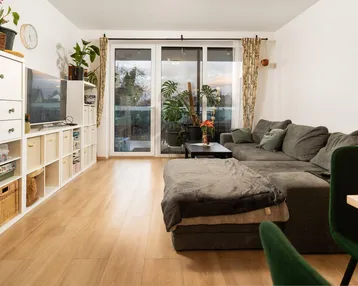 Helles Wohn-Esszimmer mit Parkettboden, großem Sofa und Zugang zum Balkon.