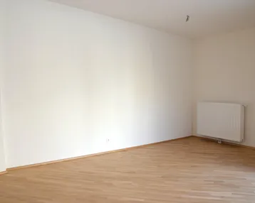 Leerer Raum mit hellen Wänden, Holzfußboden und einem Heizkörper an der Wand.