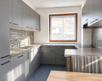 Moderne Küche mit grauen Schränken, Steinoptik-Rückwand, integrierter Sitzecke und Fenster für natürliches Licht.