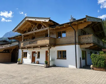 Traditionelles alpenländisches Haus mit Holzfassade, weißen Wänden und mehreren Balkonen unter blauem Himmel.