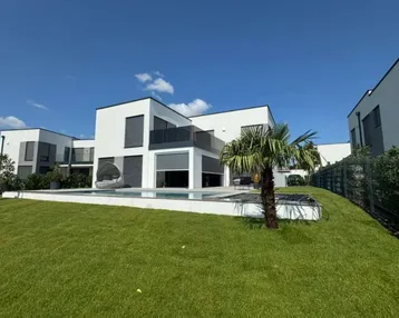 Moderne Villa mit Swimmingpool und gepflegtem Rasen unter blauem Himmel.
