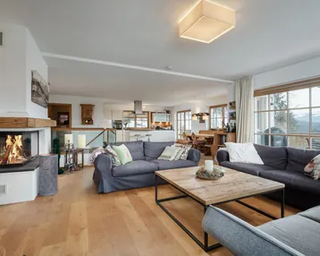Geräumiger offener Wohn- und Essbereich mit Kamin, Holzboden und Zugang zum Balkon.