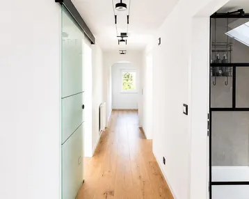 Heller Flur mit modernem Eichenparkett, Glasschiebetür und Blick in ein Badezimmer.